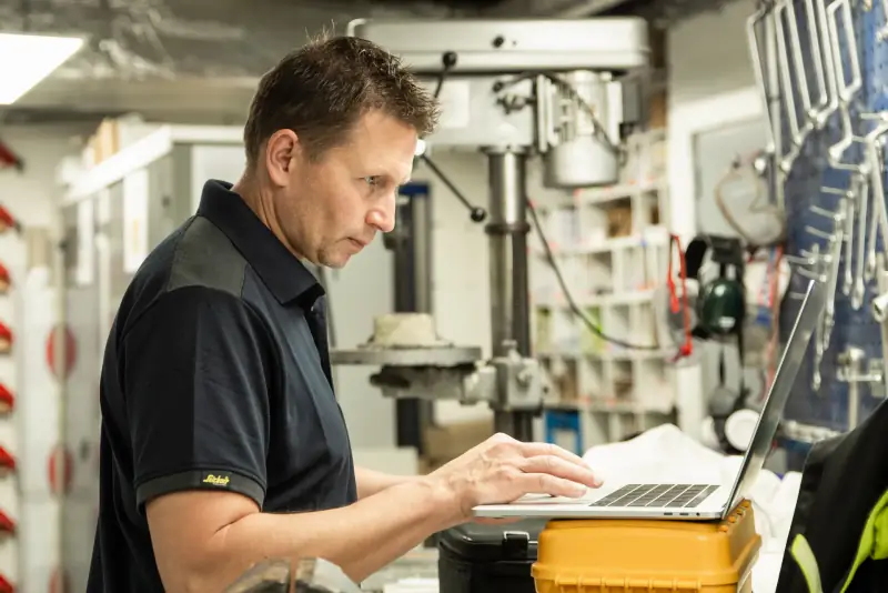 Inspecteur van Mekeur Inspectie werkt op een laptop in een werkplaats met machines