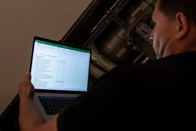 Inspecteur werkt op een laptop het keuringsrapport bij in een technische ruimte
